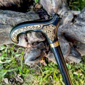 Side-view outdoor photo of the Celtic cane set against natural wood. The engraved handle glows warmly in soft light, while the dark shaft creates a polished contrast. The carved patterns and curved shape show the artisan’s precision, giving the cane a traditional yet elegant character suited for daily walking.