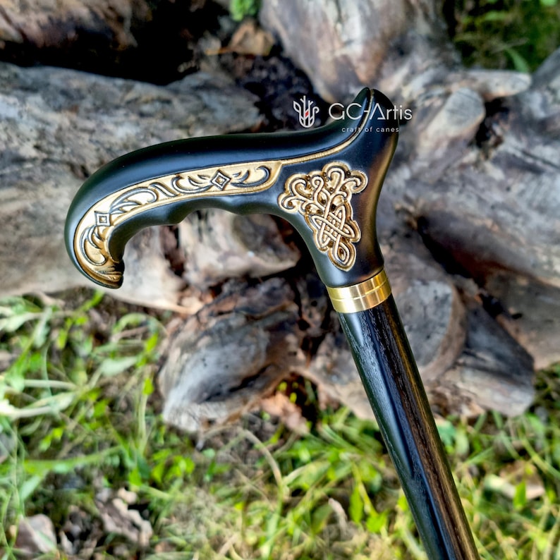 Side-view outdoor photo of the Celtic cane set against natural wood. The engraved handle glows warmly in soft light, while the dark shaft creates a polished contrast. The carved patterns and curved shape show the artisan’s precision, giving the cane a traditional yet elegant character suited for daily walking.