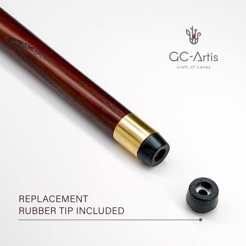 May include: A close-up of a wooden walking stick with a gold band and a black rubber tip. The walking stick is on a white background. The text "REPLACEMENT RUBBER TIP INCLUDED" is below the walking stick. A spare black rubber tip is shown to the right of the walking stick.