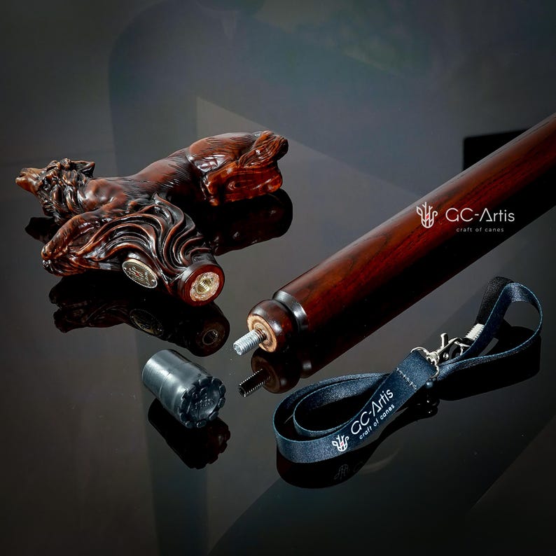 May include: A wooden walking stick with a carved horse head handle. The stick is disassembled and laid out on a black surface. The handle is a dark brown color and the stick is a lighter brown color. The stick also includes a black leather strap with a metal clasp and a black rubber tip.