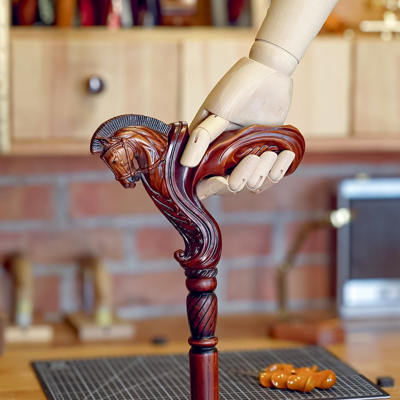 May include: A dark brown wooden walking cane featuring a detailed hand-carved horse head handle with a mane and bridle design. The shaft of the cane has a smooth, cylindrical finish with a decorative twisted pattern just below the horse head handle.
