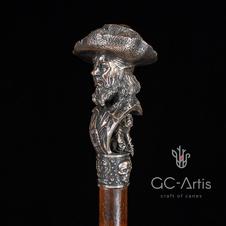 May include: A silver walking stick with a detailed bust of a pirate wearing a hat. The bust is attached to a wooden shaft with a skull and crossbones design.