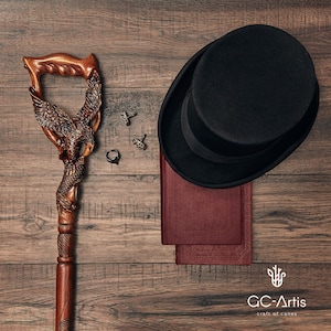 May include: A wooden walking stick with an eagle carving, a black top hat, two cufflinks, a ring, and two books on a wooden surface. The text "GC-Artis craft of canes" is visible in the bottom right corner.