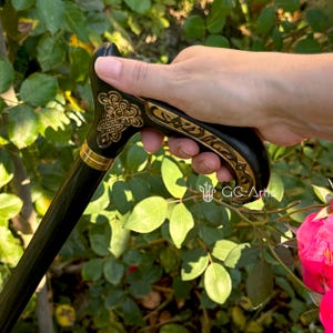 Outdoor photo of a hand holding the Celtic cane among bright green leaves. The handle fits naturally in the palm and shows the gold engraved design clearly. The scene emphasizes the cane’s comfortable grip, lightweight balance and refined artistic look.