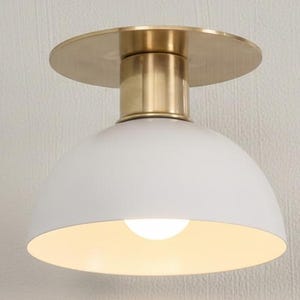 May include: A contemporary ceiling light. It features a white, domed shade and a brass-coloured base and mounting plate. The light bulb is visible inside the shade. Designed for indoor use.