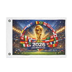 May include: A white rectangular flag featuring a vibrant graphic for the 2026 FIFA World Cup. The design includes a golden trophy, the year "2026", and a semi-circle of international flags against a stadium backdrop.