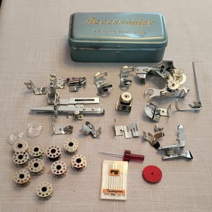 Peut inclure: Une boîte de rangement en métal bleu vintage étiquetée Accessories Sewing Machine contenant divers pieds-de-biche, accessoires, canettes en métal, un tournevis à manche rouge, un paquet d'aiguilles Tailorform et un disque en feutre rouge.
