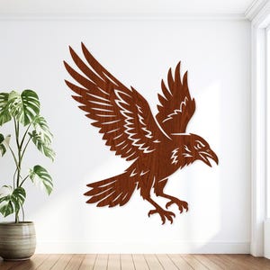 May include: A wall-mounted wooden cutout of a raven in flight with wings spread wide. The bird features a dark brown wood grain finish and is depicted with its beak open and talons extended, showcasing a detailed silhouette of a bird in motion.