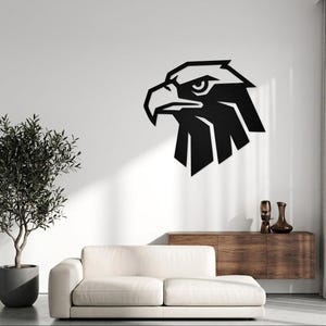 May include: A black metal wall art piece featuring a stylized, geometric eagle head profile. The design consists of sharp, angular lines and solid black shapes that form the beak, eye, and feathers of the eagle, mounted on a plain white wall.
