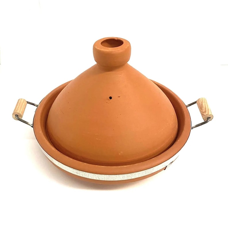 May include: A terracotta tagine pot with a conical lid and a circular base. The pot has two handles with wooden grips and a metal frame. The tagine is a traditional cooking vessel used in North African cuisine.