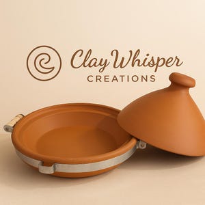 Puede incluir: Una olla de tagine de color terracota con una tapa cónica a juego. La olla está abierta. La olla tiene una banda plateada alrededor de la base y asas de madera. Se muestra el logotipo "Clay Whisper Creations".