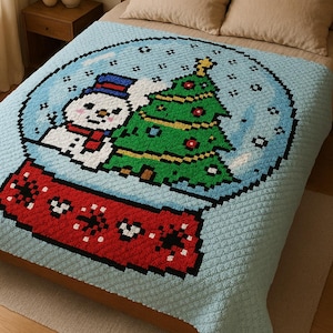 Könnte beinhalten: Eine hellblaue Decke mit einem pixeligen Design eines Schneemanns und eines Weihnachtsbaums in einer Schneekugel. Der Sockel der Schneekugel ist rot mit weißen Schneeflocken-Details. Die Decke liegt auf einem Bett mit beigen Kissen.