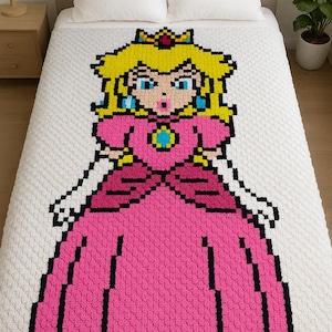 May include: A pixelated Princess Peach blanket in pink, yellow, and blue, displayed on a bed with white bedding. The blanket features a detailed image of the character, with a crown and long dress. The blanket is made of a textured material.