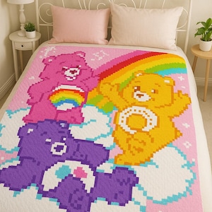 Könnte beinhalten: Eine pixelige Decke mit drei Care Bears: einem rosa Bären mit Regenbogen, einem gelben Bären mit einem Bauchsymbol und einem lila Bären. Der Hintergrund ist rosa mit weißen Wolken und einem Regenbogen.
