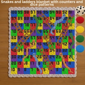 May include: A colorful, crocheted snakes and ladders blanket with a dice pattern border. The game board features numbers, snakes, and ladders. Includes crocheted dice and game piece counters in red, yellow, green, and blue. The text "Snakes and ladders blanket with counters and dice patterns" is at the top.
