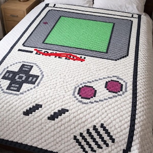 May include: A white ceramic mug with a black handle and the text "But First, Coffee" in a bold, black font. The mug is set against a blurred background, suggesting a cozy setting.