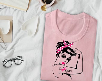 Może przedstawiać: Różowy T-shirt z grafiką przedstawiającą kobietę z różowo-białym opaską na głowie w kropki, różową wstążką na ramieniu i napisem "Hope" pod wstążką.