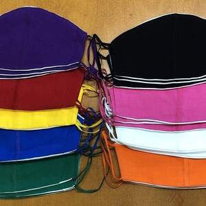 May include: A set of ten fabric face masks in various colors, including purple, red, yellow, blue, green, black, pink, white, and orange. Each mask has a white trim around the edges.