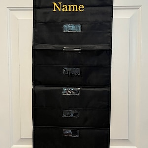 May include: Black hanging organizer with five clear pockets and the word "Name" in yellow lettering at the top.