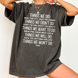 May include: Dark gray t-shirt with white text. The text includes phrases like "Things We Did," "Things We Didn't Do," and "Things We Want to Do." The shirt has a relaxed fit and short sleeves.