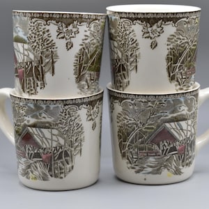 Op de afbeelding: Een set van vier crèmekleurige keramische mokken met een herhalende bruine en rode print van een overdekte brug in een winterlandschap. Elke mok heeft een cilindrisch lichaam, een gebogen handvat en een decoratieve florale rand.