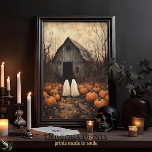 May include: A framed wall art print depicting a rustic wooden barn surrounded by a pumpkin patch with two white ghost figures standing in the centre. The scene features dark, muted tones, bare trees, and a textured, aged appearance on the print surface.