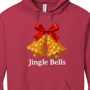 May include: A red hooded sweatshirt featuring a festive design. The design includes two golden bells with a red bow and the text "Jingle Bells" in white. The sweatshirt has a front pocket and a drawstring hood.