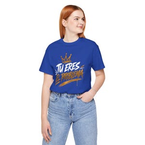 Puede incluir: Una camiseta azul real con el texto "TU ERES EL PROBLEMA" en blanco y dorado, con un gráfico de corona dorada. La camiseta está hecha de un material suave y es adecuada para uso casual.