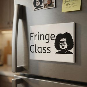 Op de afbeelding: Een witte rechthoekige magneet met de zwarte tekst "Fringe Class", vergezeld van een zwart-wit illustratie van een persoon met een bril en krullend haar. De magneet bevindt zich op een roestvrijstalen koelkast.