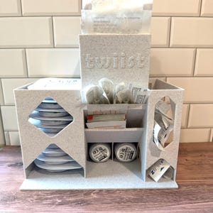 May include: A speckled white organiser with the word "twiist" embossed on the front. It features multiple compartments holding various medical supplies, including stacked circular items, small packets, and two 6 mm labelled cylindrical containers.