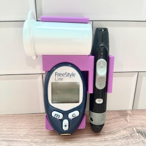 May include: A Freestyle Lite blood glucose meter with a black and purple holder, a white test strip container, and a black lancing device. The meter has a blue face with a digital display and buttons.