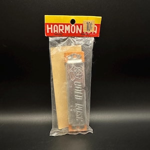 May include: A vintage Harmon brand harmonica in its original clear plastic packaging with a yellow and red header card. The harmonica features a silver metal cover plate embossed with the text 'GOLD ROSE' and a rose graphic, with wooden sides.