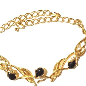 May include: A gold-toned necklace with a leaf-like design. The necklace features black gemstone accents and small clear crystals. The chain is adjustable. The jewelry is set against a white background.