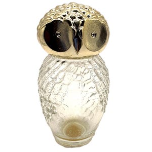 Könnte beinhalten: Eine klare Glasflasche in Eulenform mit einem strukturierten Federmuster auf dem Körper. Der Kopf ist ein glatter, reflektierender goldfarbener Metallverschluss mit zwei kreisförmigen Augen und einem spitzen Schnabel, der eine Eulenform bildet.