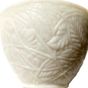 May include: A white ceramic bowl with a detailed leaf pattern. The bowl has a smooth, glossy finish and a slightly flared shape. The leaf design is raised, creating a textured surface. The bowl is likely used for serving or display.