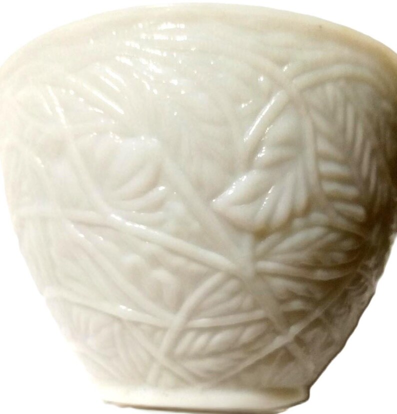 May include: A white ceramic bowl with a detailed leaf pattern. The bowl has a smooth, glossy finish and a slightly flared shape. The leaf design is raised, creating a textured surface. The bowl is likely used for serving or display.