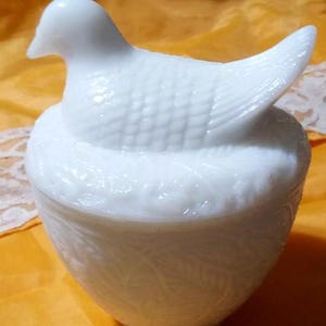 May include: A white, vintage-style trinket box shaped like a bird on a nest. The bird has detailed feathering, and the nest-shaped base features a leaf pattern. The lid lifts off to reveal the interior, perfect for storing small items.