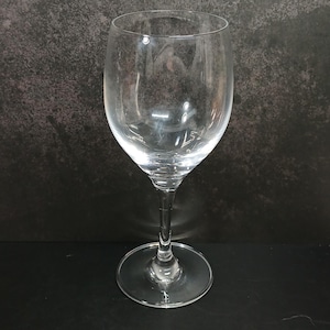 May include: A clear, stemmed wine glass with a rounded bowl and a slender stem. The glass sits on a circular base. The glass is designed for serving wine.