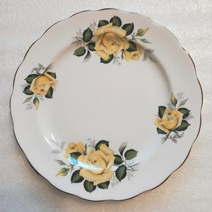 May include: White ceramic plate with a scalloped edge and a gold rim. The plate is decorated with yellow roses and green leaves. A classic design for serving food.