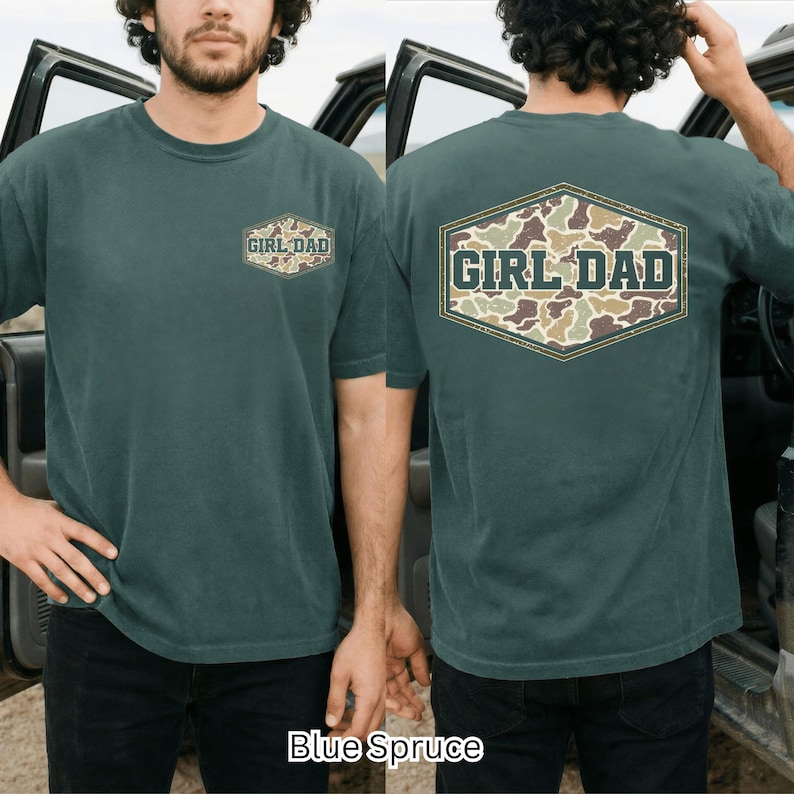 May include: Blue Spruce short-sleeve t-shirt with "GIRL DAD" text in a camouflage design. The text is on the front and back of the shirt. The shirt is a solid color with a crew neck.