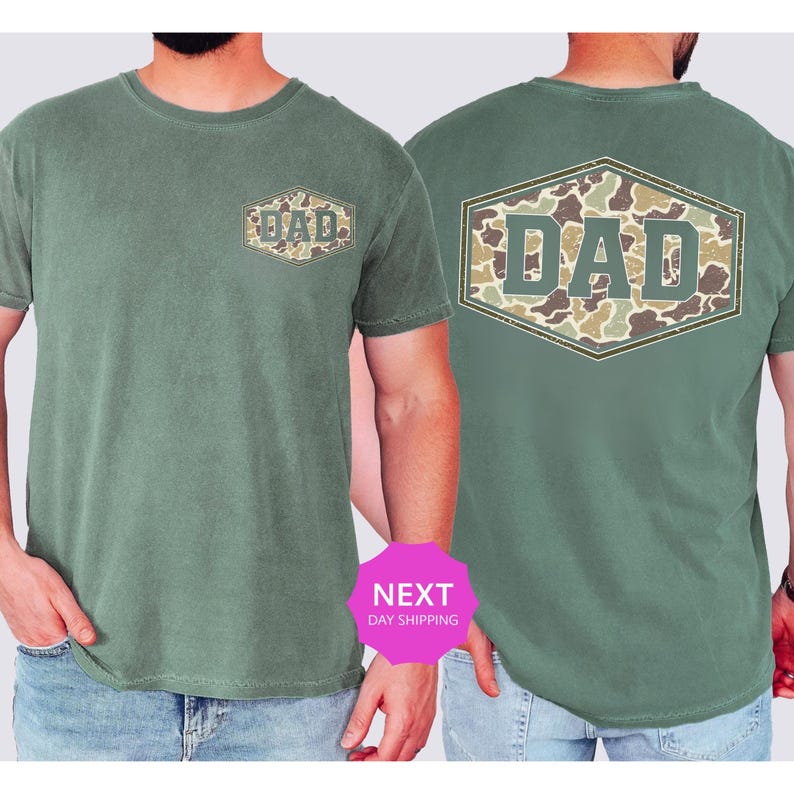 May include: Green t-shirt with a camouflage "DAD" design on the front and back. The text is in a hexagon shape. The shirt is a solid green color and has short sleeves.