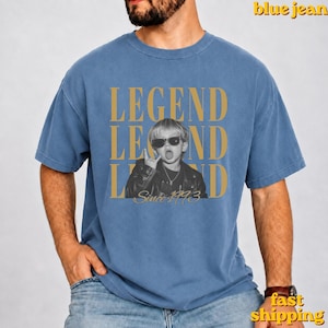 Puede incluir: Una camiseta azul de cuello redondo con una fotograf&iacute;a en blanco y negro de un ni&ntilde;o con gafas de sol y chaqueta de cuero. El texto LEGEND aparece en letras doradas grandes arriba y abajo, con la frase Since 1993 en letra cursiva dorada.