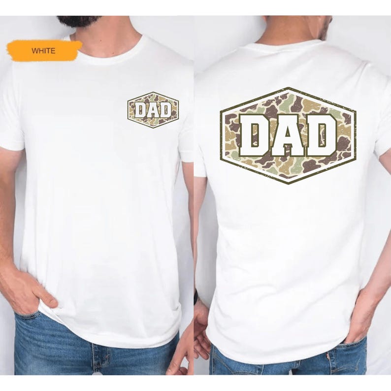 May include: White t-shirt with a camouflage "DAD" design on the front and back. The text "DAD" is in white block letters, set against a camouflage pattern within a hexagonal frame. The shirt is a classic crew neck style.