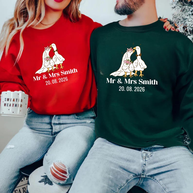 May include: Red and green sweatshirts with a wedding-themed design. Each sweatshirt features a graphic of two geese in wedding attire, with the text "Mr & Mrs Smith" and the date "20.08.2026" printed below the graphic.
