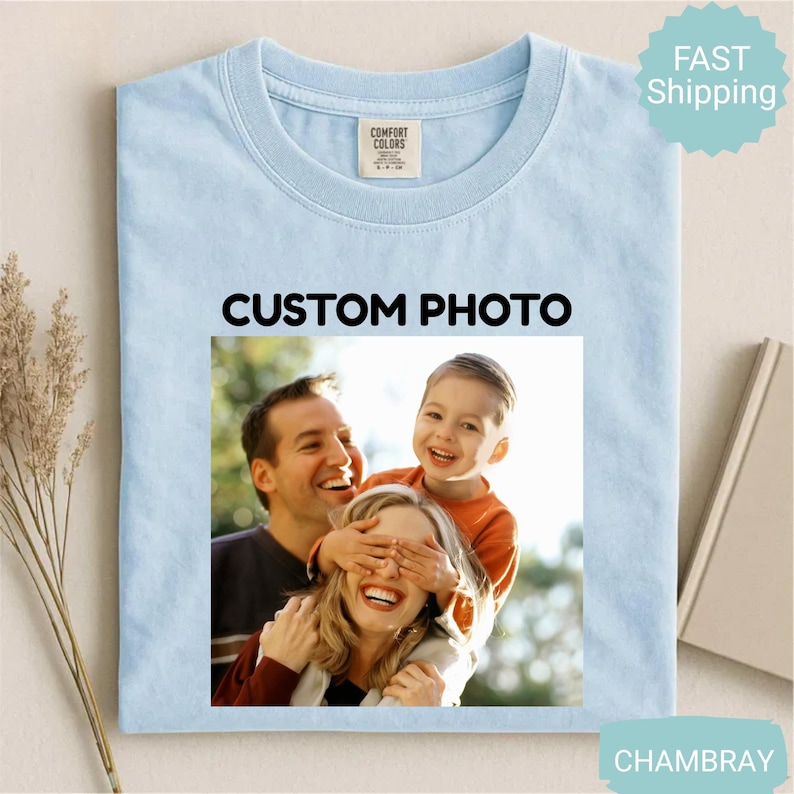 May include: Light blue t-shirt with a crew neck and a custom photo design. The photo features a family of three, with the text "CUSTOM PHOTO" above the image. The shirt is made of Comfort Colors material.