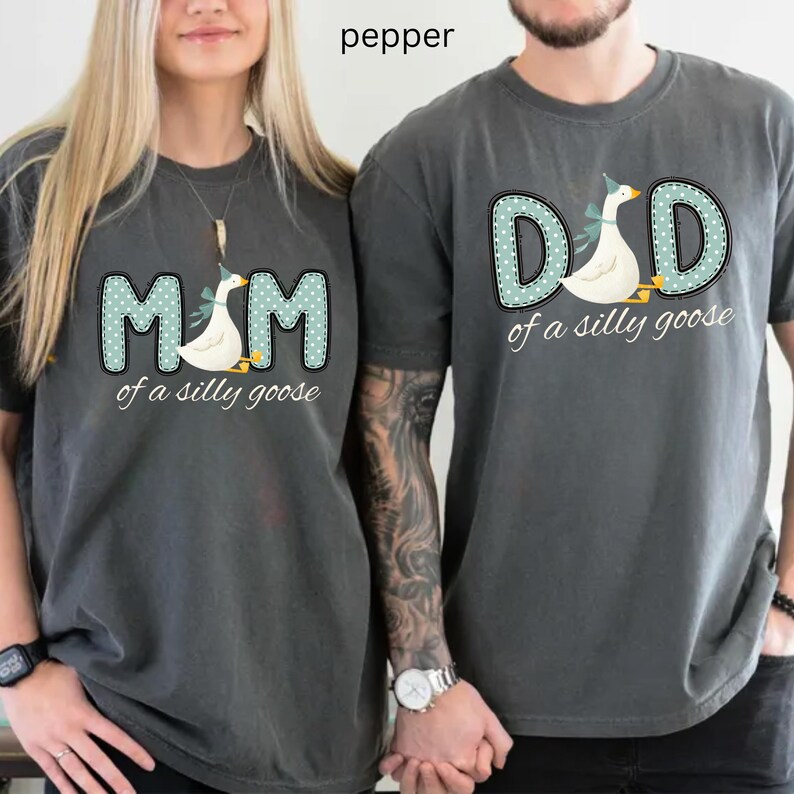 May include: Two dark gray t-shirts with matching designs. One shirt says "MOM of a silly goose" and the other says "DAD of a silly goose". Each design features a goose wearing a party hat.