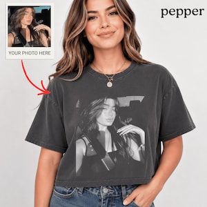 Puede incluir: Camiseta corta gris oscuro con una impresión fotográfica en blanco y negro de una persona. Una pequeña foto con el texto "YOUR PHOTO HERE" está en la esquina superior izquierda. La palabra "pepper" está impresa en negro en la esquina superior derecha.