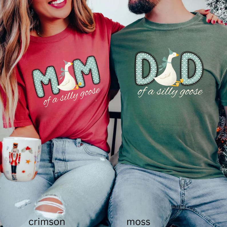 May include: Crimson and moss green t-shirts with the text "MOM of a silly goose" and "DAD of a silly goose". The text is in a blue polka dot design with a cartoon goose. The shirts are worn by two people.