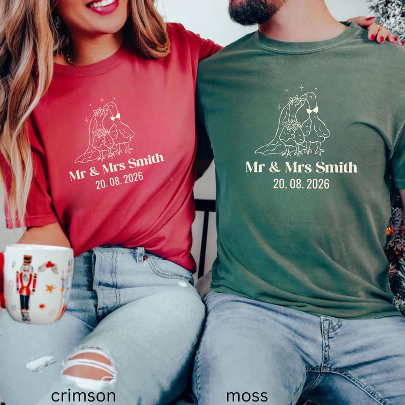May include: Crimson and moss green t-shirts with a wedding design. Each shirt features a white graphic of two birds under a veil, with the text "Mr & Mrs Smith 20.08.2026". The shirts are made of a soft material.