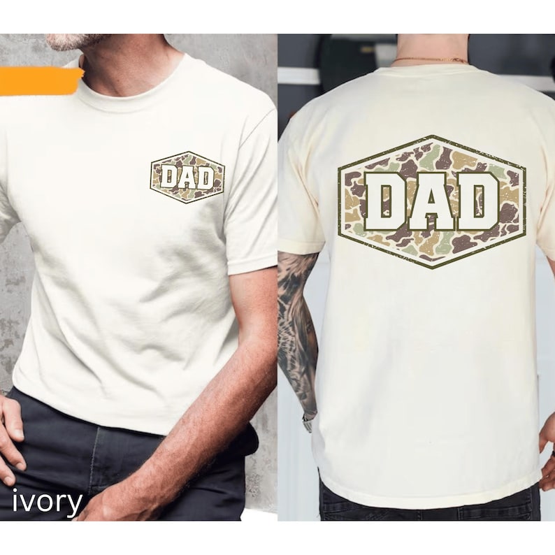 May include: Ivory-colored t-shirts with the word "DAD" in a camouflage design. The text is featured on the front and back of the shirts. The shirts have short sleeves and a crew neck.